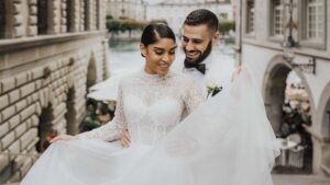 Ein Brautpaar lächelt sich an, während die Braut ihr Kleid in einer malerischen Stadtmitte präsentiert.