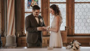 Das Paar tauscht Ringe während der Zeremonie in einem stilvollen, lichtdurchfluteten Raum mit historischen Fenstern.