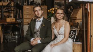 Das Paar sitzt entspannt in einer stilvollen Umgebung mit Holzmöbeln und Sonnenblumen im Hintergrund.